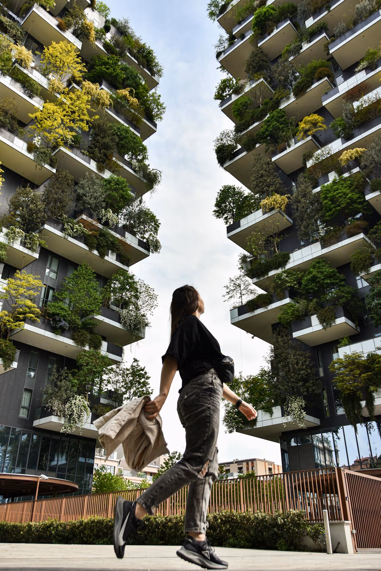 A woman walking past residential tower blocks with lush biophilic design.