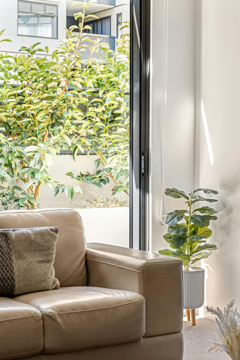 A beige leather sofa in front of a patio door looking through to a lush garden terrace beyond.