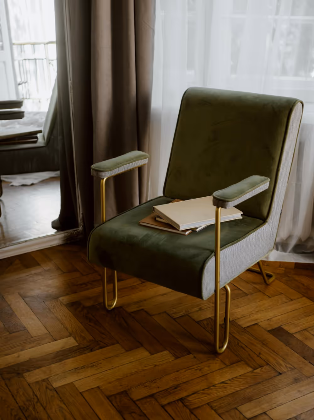 A 1970s style armchair in green velvet sitting upon a wooden parquet floor.