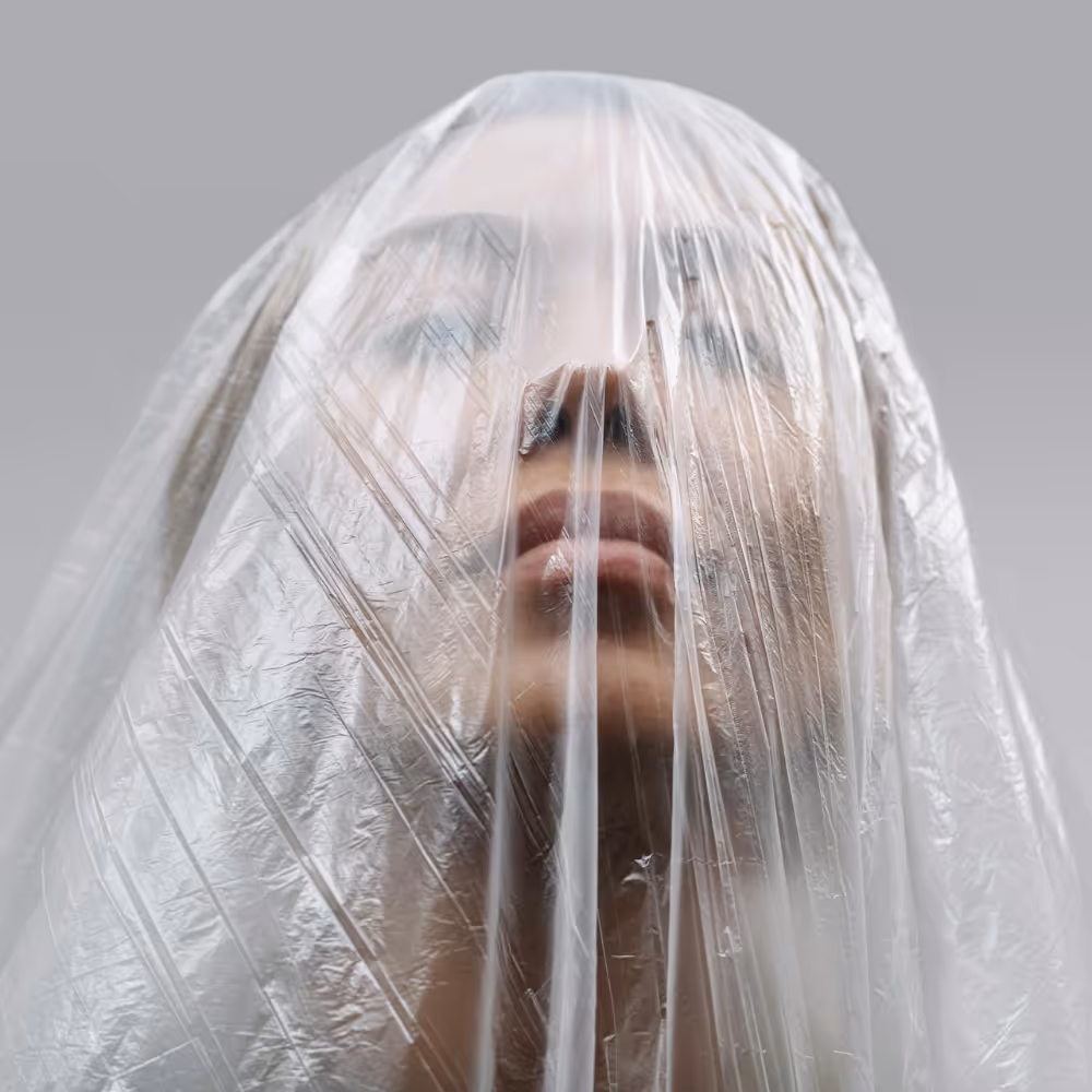 A woman's head draped in a clear plastic sheet.