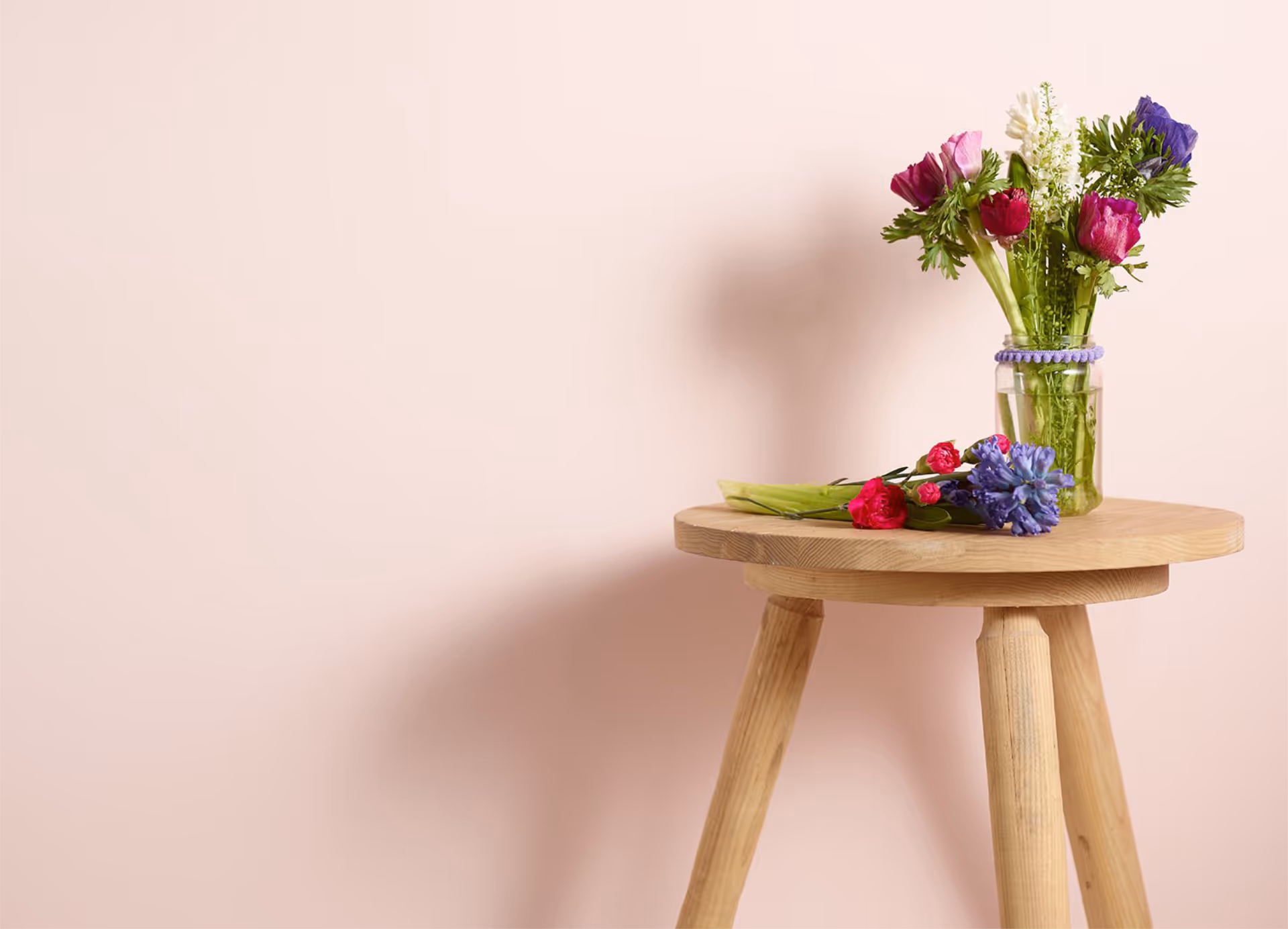 A vase of spring flowers on a wooden table in front of a blush pink painted wall.