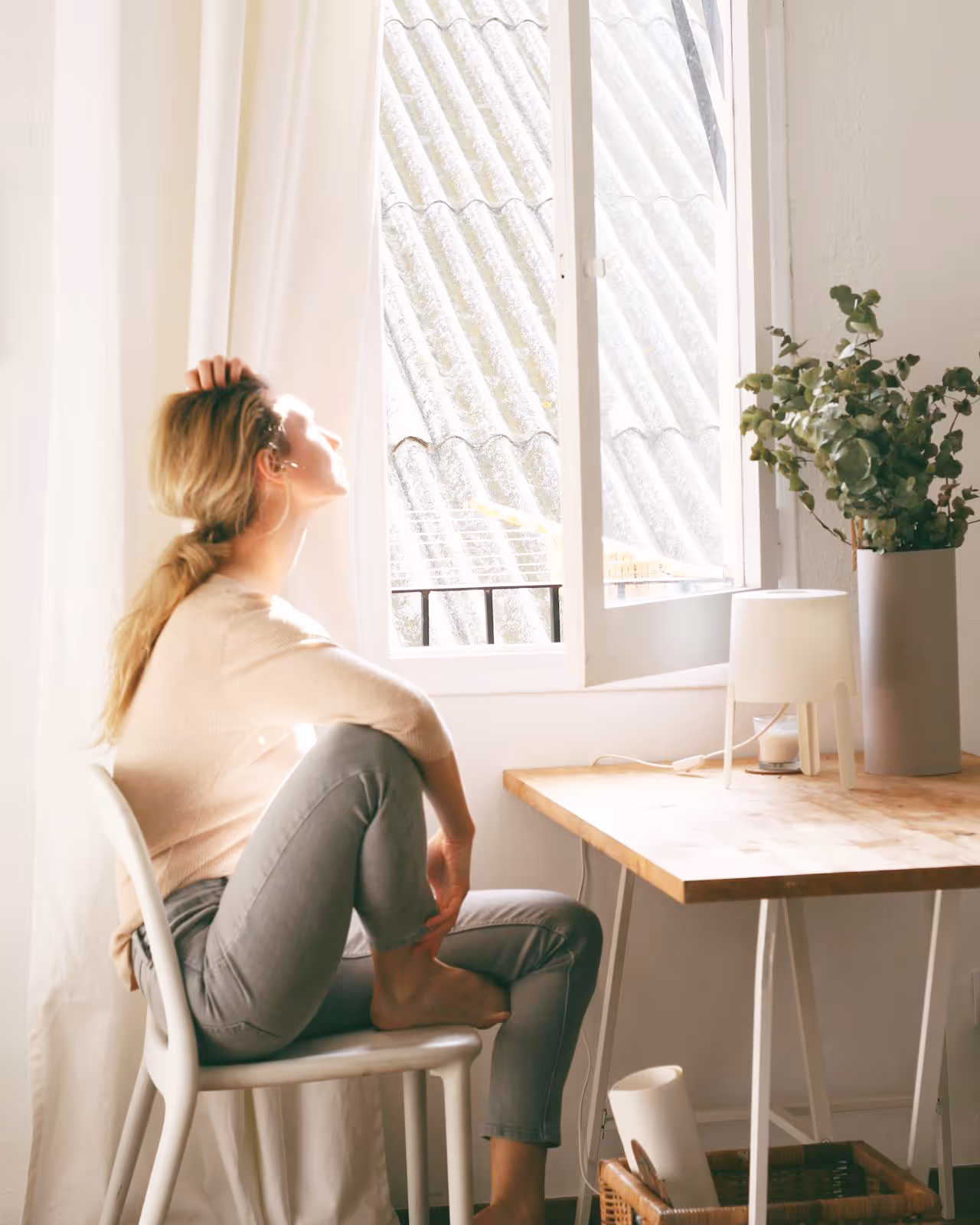 A woman sitting at a desk enjoying the warmth of sunshine through an open window.