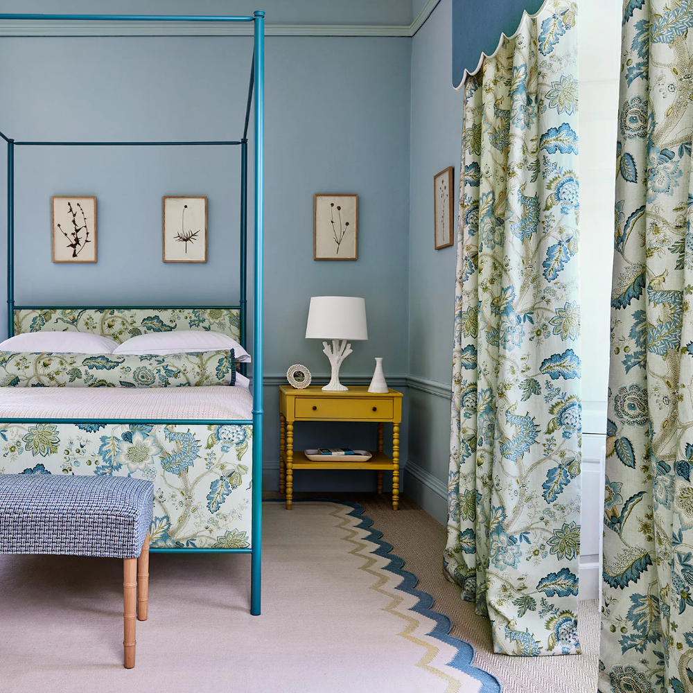 A sea blue bedroom with a blue four poster bed and floral linen curtains.