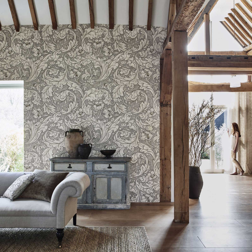 A rustic oak beamed room with a black and natural wallpaper in an acanthus design.