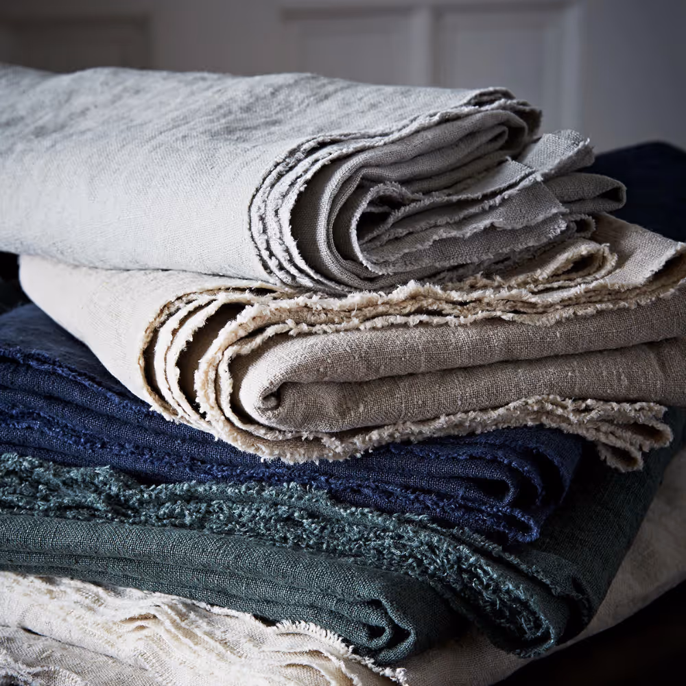 A pile of plain linen fabrics in natural tones and also navy and dark green.