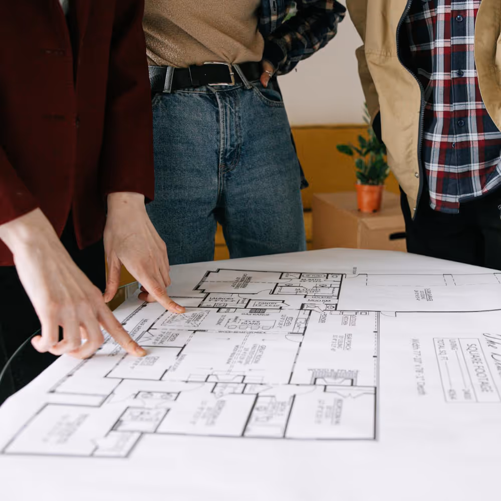 Three people stood around some architect drawings.