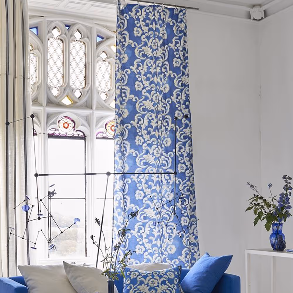 A room in a period house with white walls and furniture, and blue and white linen curtains.