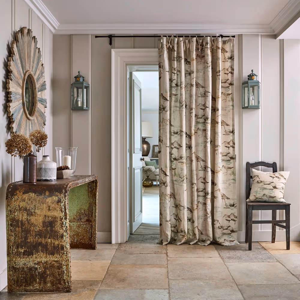 A large entrance hall with flagstone floor, reclaimed wood console table and linen curtains depicting coastal birdlife.