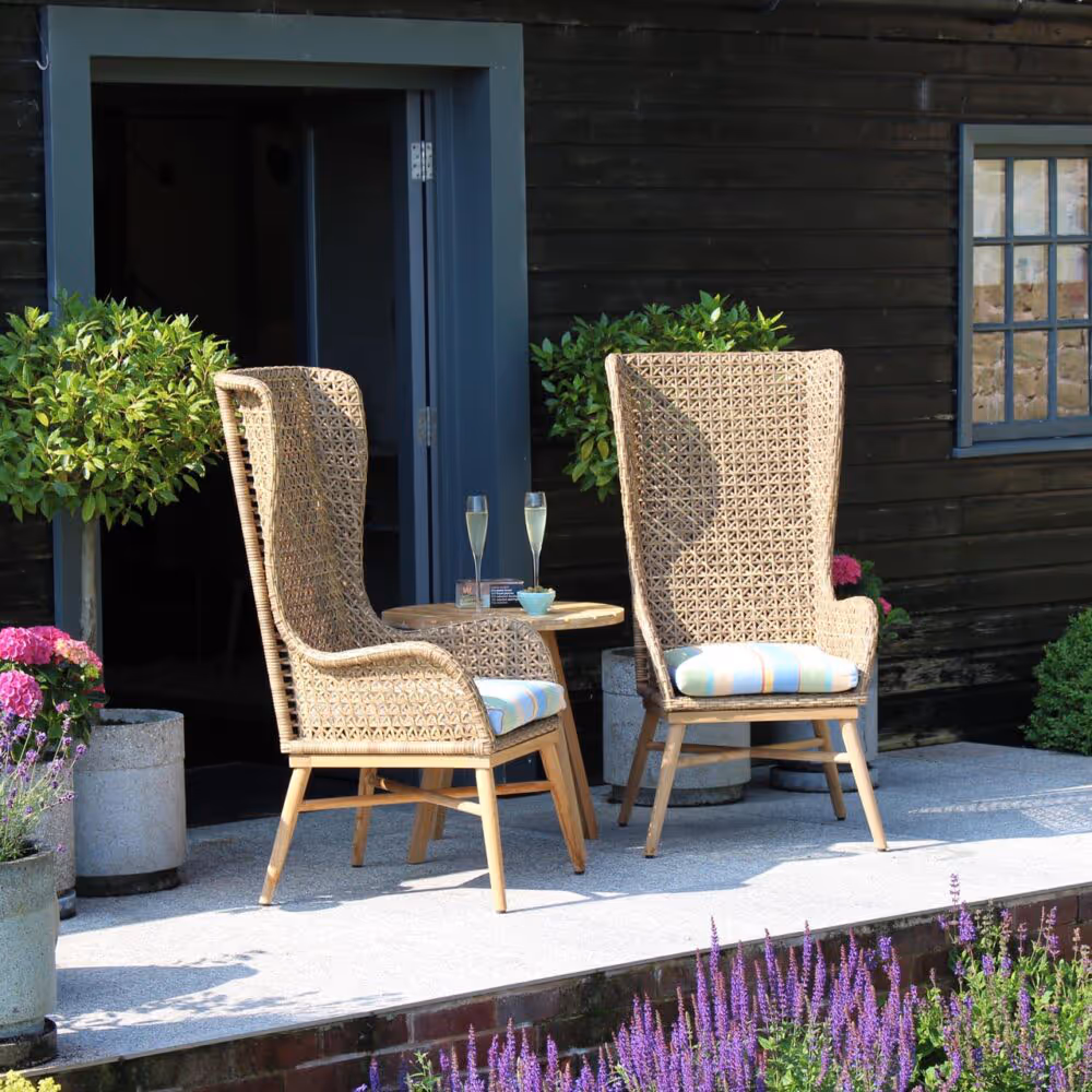 Two high back garden chairs on a patio outside a house with a dark wood clad wall.