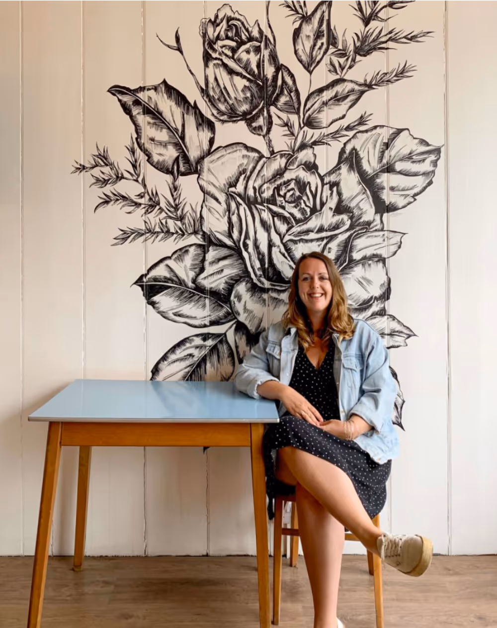 A woman sitting on a chair in front of a large line drawing of roses on the wall
