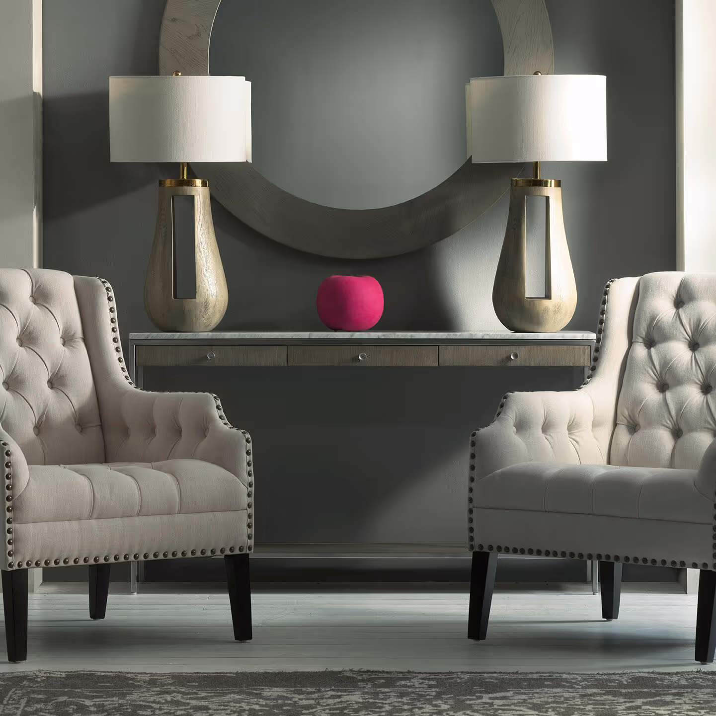 A pair of buttoned armchairs and a stone topped console table with two large table lamps.