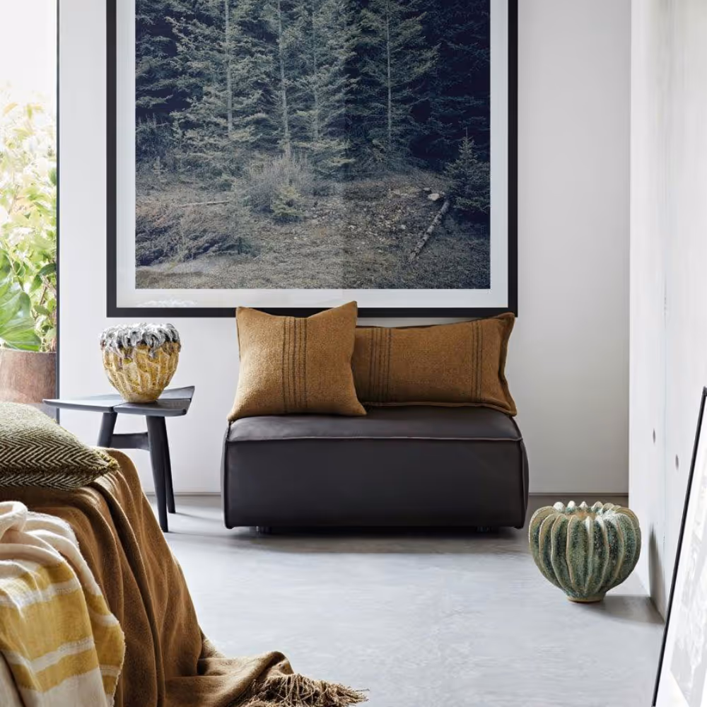 A modern room with a very large painting on the wall, fabric throws on a bed, and a chair with velvet cushions